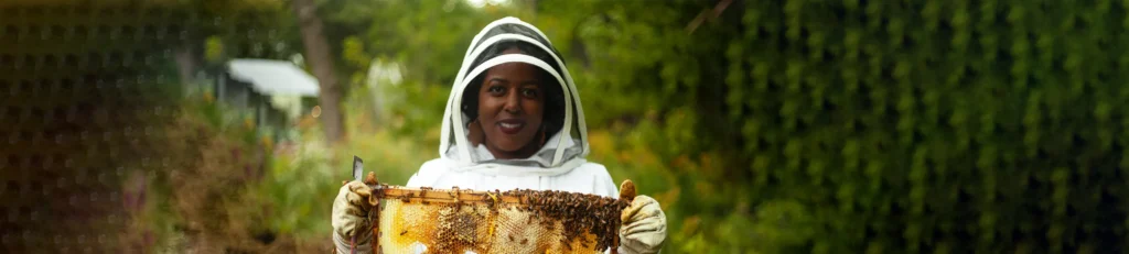 A woman in a beekeeper suit smiling and holding a hive