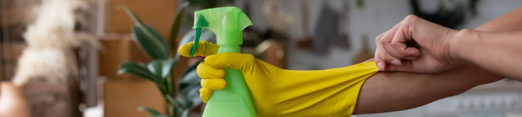A person putting on a yellow cleaning glove holding a spray bottle